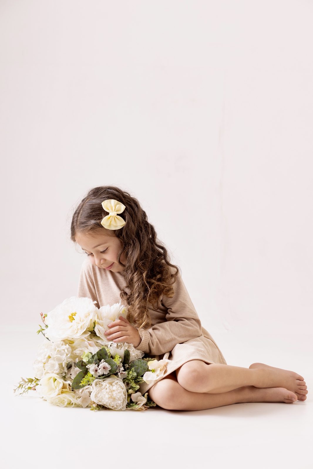 Menina com laço amarelo sentada entre flores brancas