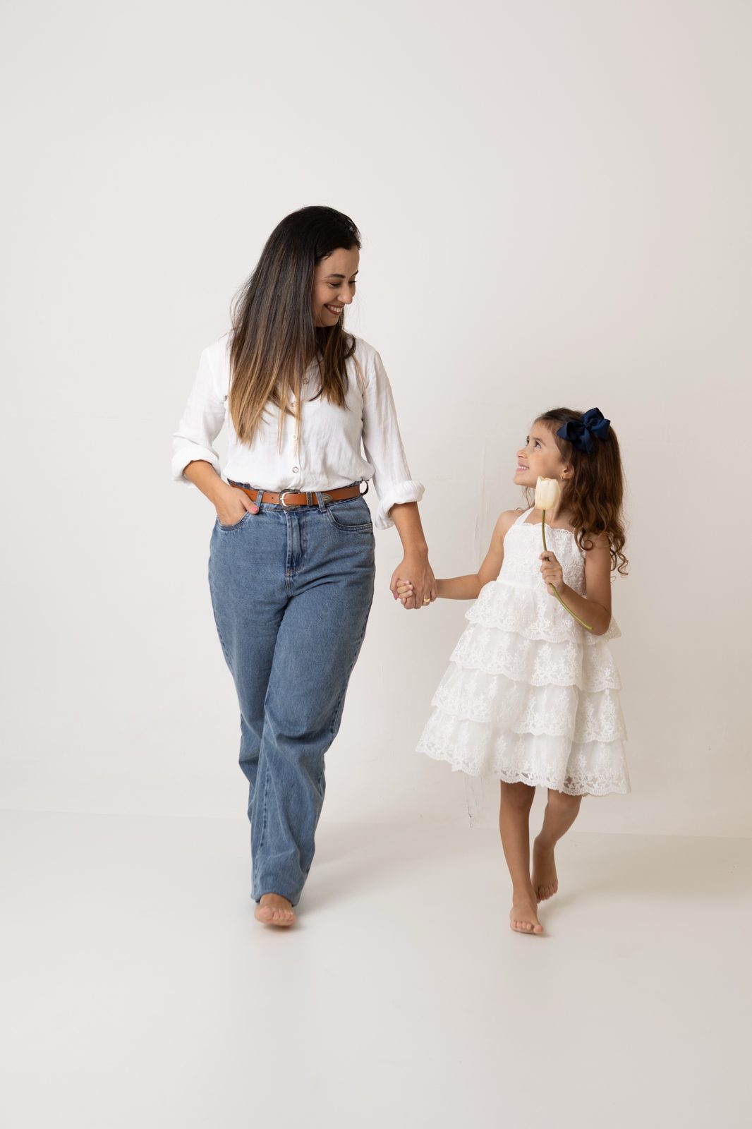 Mãe e filha de mãos dadas caminhando em fundo claro