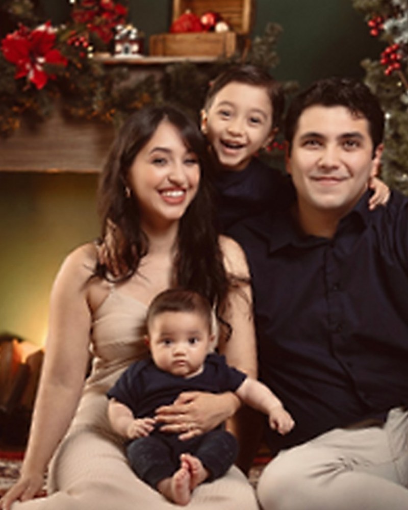 Família com duas crianças sorrindo diante da lareira decorada no cenário de Natal do Estúdio Lia